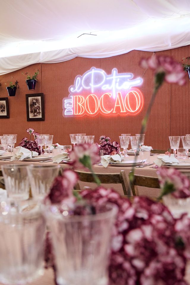 Neón «El Patio del Bocao» sobre una mesa puesta con claveles y copas